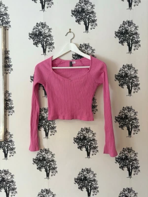 Ribbad rosa crop top med lång ärm - Trendig ribbad crop top i en härlig rosa färg från H&M. Toppen har lång ärm, fyrkantig urringning och är tillverkad i ett stretchigt material som sitter snyggt på kroppen. Perfekt för att lyfta vilken outfit som helst.