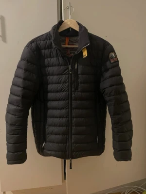 Svart dunjacka från Parajumpers - Snygg svart dunjacka från Parajumpers. Jackan har dragkedja framtill, bröstficka med dragkedja och klassisk PJS-logga på ärmen. Perfekt för kalla vinterdagar och vårkvällar, funkar året om egentligen och riktigt stilren look.