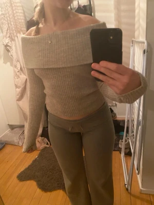 Beige off shoulder stickad tröja - Trendig beige stickad tröja med bred off shoulder-krage och ribbad struktur. Långa ärmar och figurnära passform, perfekt för en stilren och mysig look. Materialet känns mjukt och stretchigt, vilket gör den bekväm att bära hela dagen. Endast använd en gång, och tillkommer inga defekter eller skavanker.