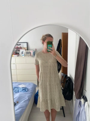 Blommig grön klänning med volang - Söt, kortärmad, grön klänning med småblommigt mönster och volangkant nertill. Klänningen är helt oanvänd med lappen kvar.