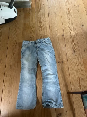 Ljusblå bootcut jeans - Säljer ett par ljusblå bootcut jeans med klassisk femficksmodell och låg midja. Jeansen har en avslappnad passform och är tillverkade i denim med lätt slitningar framtill för en cool vintagekänsla. Perfekta för en casual look.