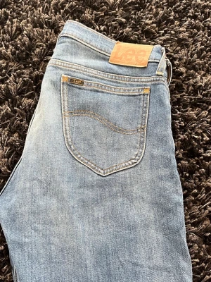 Ljusblå jeans från Lee - Säljer ett par klassiska ljusblå jeans från Lee med femficksmodell och snygga kontrastsömmar. Jeansen har en avslappnad passform och är perfekta för en casual look. Ikonisk Lee-lapp bak i midjan och diskret logga på bakfickan. Hör av er vid funderingar! 