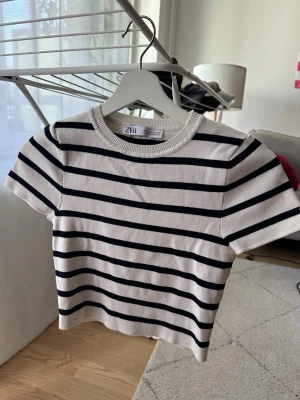 Randig topp från Zara i bomull - Kortärmad topp från Zara i vit med svarta ränder. Klassisk rund halsringning och ribbad kant. I ett stickad liknande material. Använd ett fåtal gånger så den är i superbra skick. Storlek M men mer lik S