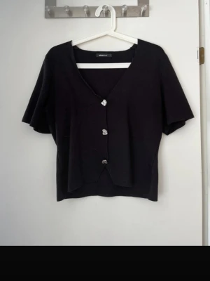 Svart kortärmad topp från Gina Tricot - Svart kortärmad topp från Gina Tricot med v-ringning och tre dekorativa knappar. Storlek L men passar mindre också 