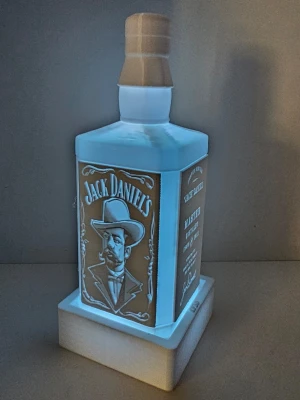 Jack Daniel's flaska LED-lampa - Dekorativ 3D-printad Jack Daniel’s-flaska med RGB-belysning och fjärrkontroll. Lampan lyser upp flaskan snyggt och kan ändra färg, vilket gör den perfekt som dekoration i rum, barhörna, gaming setup, mancave eller på en hylla.  RGB-lampan har flera färger och ljuslägen, bland annat rött, grönt, blått, vitt, flash, strobe, fade och smooth. Flaskan står i en 3D-printad bas/hållare och lampdelen kan tas ur.   Ingår: 3D-printad Jack Daniel’s-flaska 3D-printad bas/hållare LED-lampa Fjärrkontrol 
