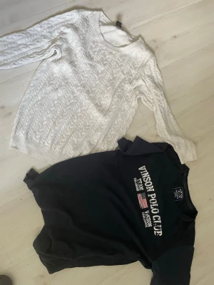 Vit kabelstickad tröja & Vinson Polo Club sweatshirt - Två tröjor: en vit kabelstickad tröja med rund hals och långa ärmar, samt en svart sweatshirt från Vinson Polo Club med tryck och amerikansk flagga på bröstet. Perfekt för dig som gillar klassisk och sportig stil. T-shirt står L men är met som M
