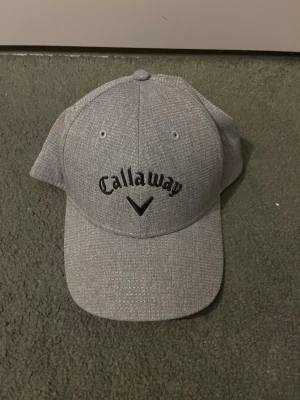 Grå keps från Callaway - Snygg grå keps från Callaway med böjd skärm och svart broderad logga framtill. Klassisk sexpaneldesign med ventilationshål och justerbar baksida. Perfekt för dig som gillar sportig och stilren look. Aldrig använd bara provtestat.                                                                    Bara att skriva om du har några frågor eller vill ha fler bilder!