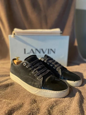 Navy Lanvin sneakers i mocka och lack - Snygga navysneakers från Lanvin i mocka och lackad tå. Skorna har vita sulor och navy skosnören. Klassisk låg modell som passar perfekt till streetwear och trendiga outfits. Kommer med originalkartong och dustbag. Har ni några frågor så är det bara att fråga! Storlek: 43/ UK8