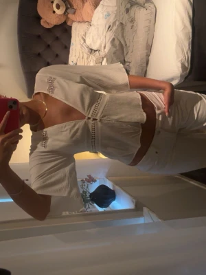 Vit blus med spetsdetaljer - Säljer en söt vit blus med v-ringning och spetsdetaljer vid axlar och bröst. Blusen har trekvartsärm, lätt croppad passform och knäppning framtill. Perfekt till jeans eller kjol för en fräsch look.