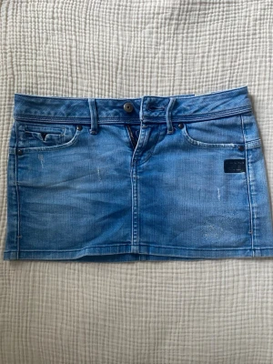 Blå jeanskjol från G-Star  - Snygg blå jeanskjol från G-star. Kjolen har en kort passform och är tillverkad i denim med ljusa slitningar för en cool look. Perfekt att matcha med sneakers eller boots.