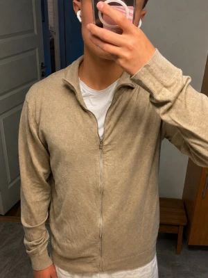 Beige ziptröja med krage slim fit från Lindbergh - Snygg beige ziptröja med krage och långa ärmar i slim fit Tröjan har en enkel och stilren design med ribbade muddar vid ärmslut och nederkant. Perfekt att slänga på sig över en t-shirt för en avslappnad look.