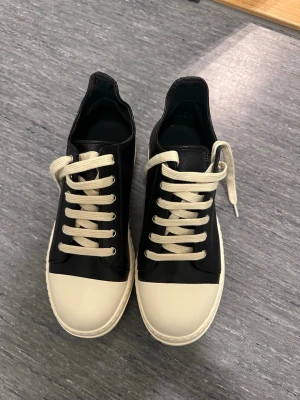 Rick owens - Rick owens Snygga svarta sneakers med kontrasterande vit tå och sula samt vita skosnören. Skorna har en klassisk låg profil och är tillverkade i slätt material som ger en clean look. Perfekta för dig som gillar minimalistisk stil.