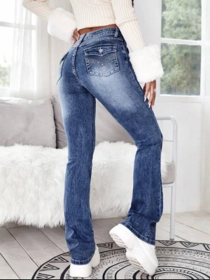 Mörk blåa bootcut jeans med detaljer - Snygga blå bootcut jeans med slitningar och dekorativa nitar på bakfickorna. Jeansen har klassisk femficksdesign och markerad tvätt för en trendig look. Perfekta för dig som vill ha en cool och avslappnad stil.