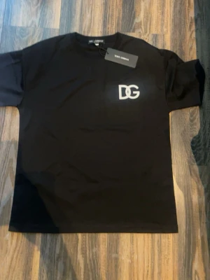 Svart DG t-shirt från Dolce & Gabbana - Snygg svart t-shirt från Dolce & Gabbana med DG-logga i vitt på bröstet. Klassisk rund hals och korta ärmar. Perfekt basplagg med stilren design och skön passform.