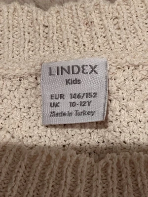 Vit stickad topp från Lindex - Snygg vit stickad topp från Lindex med dekorativt hålmönster nedtill och på ärmarna. Modellen har cold shoulder-detaljer och ribbad halskant. Perfekt för dig som gillar en trendig och luftig stil.