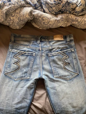 Ljusblå jeans från Wrangler - Säljer ett par ljusblå jeans från Diesel med klassisk femficksdesign och snygga kontrastsömmar på bakfickorna. Jeansen har en rak passform och är tillverkade i denim med en lätt tvättad look. Perfekta för en avslappnad stil.