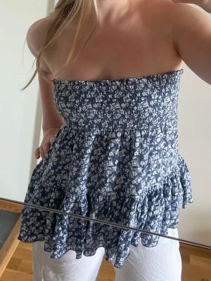 Blommig blå volangkjol - Supersöt kort kjol i blått med vitt blommönster och volangkant. Funkar även att använda som topp!! Endast använd en gång då jag har så många kjolar haha💕