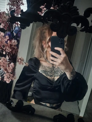 Svart croppad topp med puffärm - Trendig svart croppad topp med puffiga långärmar och snygg v-ringning. Toppen har en lätt glansig finish och sitter tight över kroppen. Perfekt för dig som vill ha en edgy och stilren look.