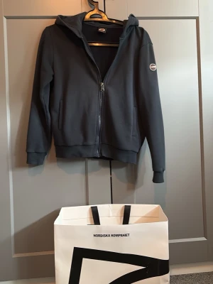 Mörkblå hoodie från Colmar - Snygg mörkblå hoodie från Colmar med dragkedja framtill och huva. Klassisk design med två fickor och Colmar-logga på ärmen. Perfekt för en avslappnad och sportig stil. Mjukt material som känns skönt mot huden. Tröjan är köpt på nk i Göteborg för ungefär 1 år sedan kvitto och allt ingår tveka inte på att skriva om ni funderar på något😁