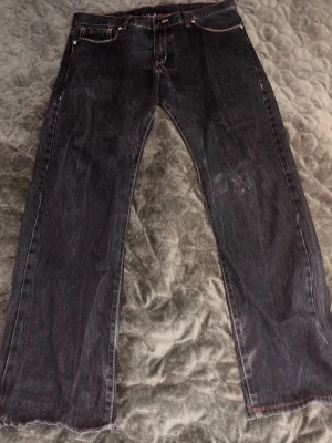 Christian Audiger - Säljer ett par svarta jeans med rak passform och slitna detaljer vid bensluten. Jeansen har klassiska fem fickor och kontrastsömmar. Snyggt mönster på bakfickorna ger extra edge. Perfekta för dig som gillar en lite tuffare stil.