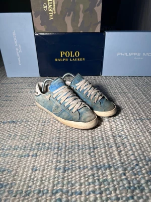 Blå Philippe Model sneakers i mocka - Snygga blå sneakers från Philippe Model med ovandel i mocka och detaljer i vitt. Skorna har vita snören, lågt skaft och en klassisk siluett. Perfekta för dig som gillar en stilren och trendig look.