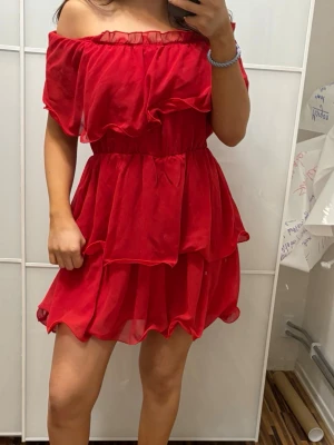 Röd off shoulder volangklänning - Säljer en superfin röd klänning med off shoulder-modell och volanger. Klänningen har resår i midjan och är gjord i ett lätt, luftigt tyg som ger en flowy känsla. Perfekt för dig som vill sticka ut med en färgstark och trendig look.
