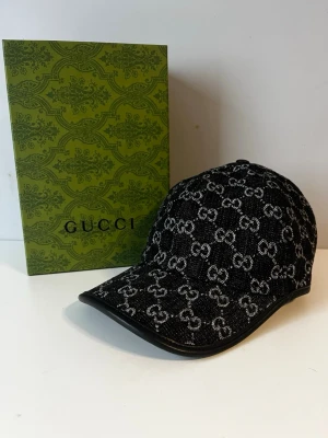 Svart Gucci Keps - Snygg svart keps från Gucci med klassiskt GG-monogram i svart/grått över hela kepsen. Kepsen är i princip i nytt skick. Fråga vid intresse
