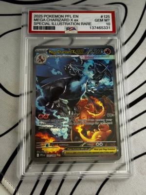 PSA 10 Mega Charizard X ex Pokémonkort - Säljer ett grymt samlarkort, Mega Charizard X ex, special illustration rare från 2025 Pokémon PFL EN. Kortet är graderat PSA 10 GEM MT och ligger i skyddande plast. Färgstark design med svart och blå Charizard och eldiga detaljer. OBS KORTET ÄR FEJK