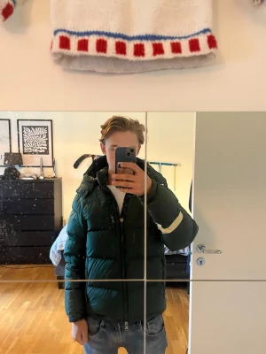 Mörkgrön pufferjacka Polo Ralph Lauren - Snygg mörkgrön pufferjacka från Polo Ralph Lauren med hög krage och dragkedja framtill. Jackan har en klassisk pufferdesign och är perfekt för kalla vinterdagar. Märket syns tydligt på insidan och jackan har en sportig vibe. Litet hår på ena armen, lätt att fixa. Kanonpris. Hör av er om ni funderar över något.