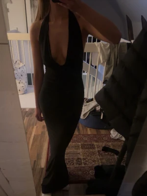 Svart långklänning med öppen rygg - Snygg svart långklänning med djup urringning och halterneck. Klänningen har en tight passform och öppen rygg med knyt i nacken. Jag är 174cm och den går hela vägen ner på mig💗Har aldrig andvänt klänningen och prislappar är kvar💘