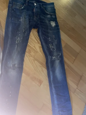 Blå slitna skinny dsquared 2 jeans  - Säljer ett par blå dsquared 2 skinny jeans med slitningar och hål på framsidan färgglad patchdetalj bak. Jeansen har klassisk femficksdesign och är tillverkade i denim med stretch. Perfekta för en cool och avslappnad streetstil.