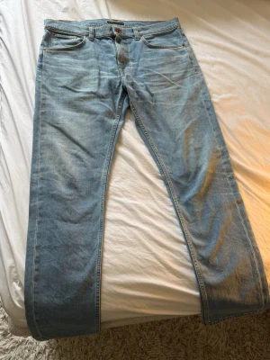 Ljusblå raka jeans från Nudie Jeans - Säljer ett par ljusblå jeans från Nudie Jeans med klassisk rak passform. Jeansen har fem fickor, subtila slitningar och en patch i läder baktill i midjan. Tillverkade i bomull med snygg tvättad look och kontrastsömmar.