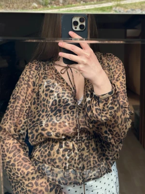 Leopardmönstrad blus från NA-KD - Snygg transparent blus från NA-KD med leopardmönster. Blusen har långa ärmar, knytning vid halsen och resår i midjan för en feminin siluett. Perfekt för dig som vill sticka ut med ett djurmönstrat plagg.