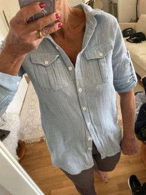 Blåvit randig skjorta med knappar - Snygg blåvit randig skjorta med klassisk krage och vita knappar hela vägen. Skjortan har två bröstfickor med lock och långa ärmar som kan rullas upp och fästas. Den är jätteskönt på kroppen 
