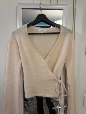 Beige omlottkofta från Gina Tricot - Mysig beige stickad omlottkofta från Gina Trict. Perfekt för lager-på-lager och enkel att styla till olika outfits. Har aldrig använt 💗