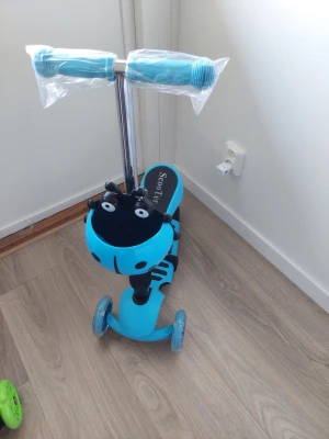 Blå sparkcykel med djurmotiv - Säljer en blå trehjulig sparkcykel med svart djurmotiv framtill och texten 'ScooTer' på fotplattan. Styret är justerbart och har blå handtag i plast. Hjul och ram är i plast och metall, perfekt för yngre barn som vill ha kul utomhus.