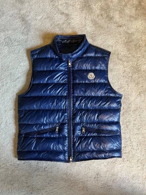 Moncler gui väst  - Säljer nu min nästan helt nya marinblåa Moncler gui väst i storlek S men passar nästan som M. Själv klart äkta och pris går absolut att diskutera!!⚜️🌊