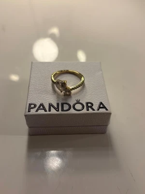 Guldfärgad ring med stenar från Pandora - Snygg guldfärgad ring från Pandora med två stora, gnistrande stenar i olika former. Ringen har en tvinnad design som ger en cool och modern känsla. Perfekt accessoar för att lyfta din stil.
