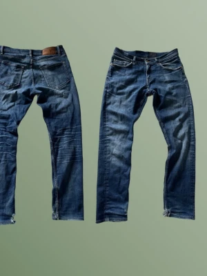 Blå tiger of sweden jeans - Säljer ett par blå jeans med raka ben och slitna detaljer vid benslut och knän. Jeansen har klassisk femficksdesign och snygga ljusa tvättade partier. Perfekta för en avslappnad och trendig look.