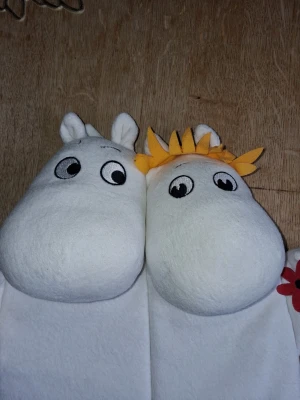 Mumin och Snorkfröken spjälsängsdekoration - Spjälsängsdekoration i form av Mumin och Snorkfröken, tillverkade i mjukt tyg. Snorkfröken har gult hår och håller en röd blomma, båda har broderade ögon och detaljer. Perfekt för lek eller som dekoration för Mumin-fans.
