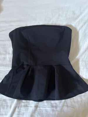 Svart och vit topp från HM!! - Två snygga axelbandslösa toppar i svart och vitt med peplumvolang nedtill. Perfekta för att skapa en trendig look. Tillverkade i ett slätt bomullstyg som ger en stilren känsla. Passformen är figurnära upptill och utsvängd nedtill.