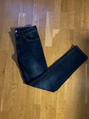 Mörkblå slim fit jeans från RYVLS - Snygga mörkblå slim fit jeans från RYVLS med klassisk femficksdesign och kontrastsömmar. Jeansen har en stilren tvätt. Köpts slitningar på alla fickorna. Har endast använt ett fåtal gånger