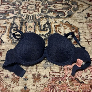 Mörkblå spets-bh med rosett - Oanvänd Hunkemöller bygel-bh i mörk blå! Bh:n är i storlek 75E och har bara blivit testad. Super skön under en vanlig T-shirt men väldigt snygg också under en mesh tröja!🪩