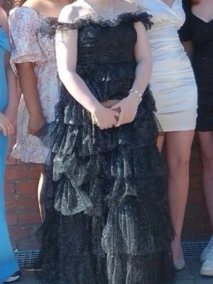 Balklänning  - Supersnygg svart långklänning från Mascara med glittrigt tyg och volanger. Offshoulder-modell med romantiska detaljer och flera lager i kjolen som ger extra volym. Perfekt för dig som vill sticka ut på bal eller fest! 💫