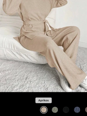Beige ribbat loungewear-set - Mysigt loungewear-set i ribbat material med vida byxor och matchande långärmad topp. Setet är aprikosbeige och har ett knytband i midjan för extra passform. Perfekt för en avslappnad och trendig look hemma.