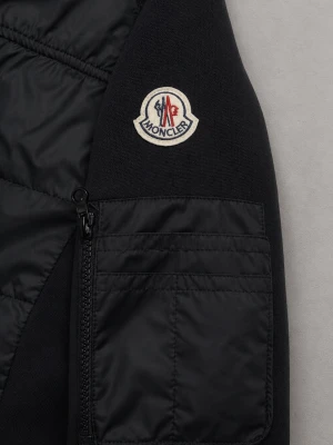 Svart Moncler pufferjacka med huva - Svart pufferjacka från Moncler med huva, quiltad front och ärmficka med dragkedja. Jackan har Moncler-logga på ärmen och ribbade muddar med rödvita detaljer. Perfekt för dig som vill ha en stilren och sportig look.