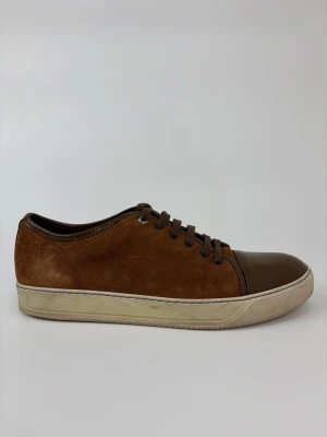Bruna Lanvin sneakers i mocka och läder - Snygga bruna sneakers med ovandel i mocka och tåparti i brunt läder. Skorna har vita sulor och matchande bruna skosnören. Perfekta för dig som gillar en stilren och klassisk look med en twist av olika material.