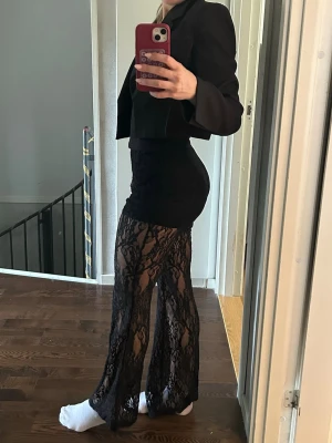 Svarta spetsleggings med utsvängda ben - Säljer ett par svarta leggings i genomskinlig spets med blommigt mönster och utsvängda ben. De har hög midja och sitter tight upptill för en snygg siluett. 