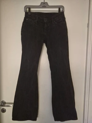 Svarta bootcut jeans - Säljer ett par svarta bootcut jeans med klassisk femficksdesign och normalhög midja. Jeansen har utsvängda ben och är tillverkade i denim. Det står storlek 24/32 men jag upplever Dessa som 24/30.
