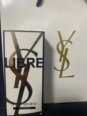 Yves Saint Laurent Libre Le Parfum - Säljer en lyxig parfym från Yves Saint Laurent, Libre Le Parfum. Förpackningen är vit med stora guldiga och svarta detaljer samt YSL-loggan. Perfekt för dig som gillar exklusiva och trendiga dofter.